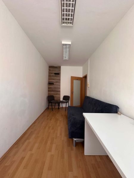 Na prenájom menšia  kancelária v centre mesta DS - 12,94 m2 - Interiér kancelárie s pohovkou, stolom a podlahou s dreveným dekorom.