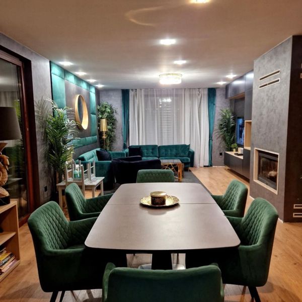 Znížená cena    Luxusný 4-izbový rodinný dom s letnou kuchyňou a nádhe - Jedálenský stôl so zelenými stoličkami, krb, pohovka a podlaha s dreveným dekorom.