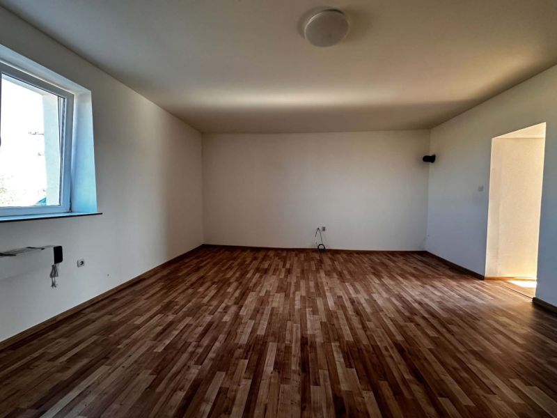 Na predaj 2-izb. byt v dvojdome (110 m²) v štandarde s krbom – Možnosť - Prázdna miestnosť v rodinnom dome s podlahou s dreveným dekorom a veľkým oknom.