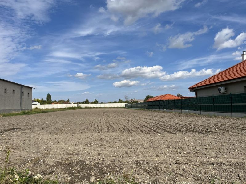 ZNÍŽENÁ CENA! Veľký, 2038 m2 stavebný pozemok v Holiciach! - Pozemky - bývanie v Holiciach, medzi domami s červenými strechami a modrou oblohou.
