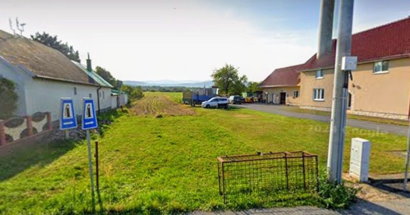 Pozemok na predaj - Pozemky - bývanie v Sačurove s trávnatou plochou a vidieckymi budovami na pozadí.