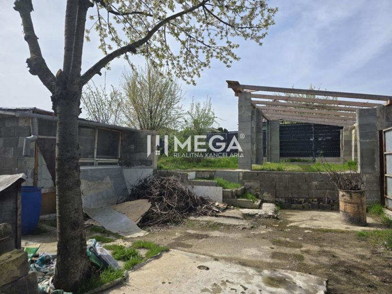 VÝRAZNÁ ZĽAVA rozostavaná stavba, Sokoľany - Košice okolie - Dvor rodinného domu v Sokoľanoch so stromom, stavebným materiálom a nedokončenou stavbou.