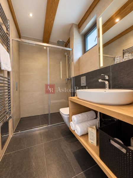 Predaj! INVESTUJTE DO MIESTA, KAM SA ĽUDIA VRACAJÚ – TATRALANDIA - Moderná kúpeľňa so sprchovacím kútom a podlahou s dreveným dekorom v rodinnom dome.
