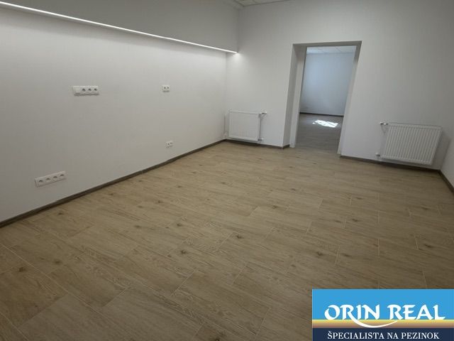 Na prenájom obchodný priestor v centre Pezinka 100m2 - Obchodné priestory s podlahou s dreveným dekorom, biele steny a radiátory.