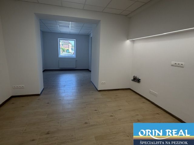 Na prenájom obchodný priestor v centre Pezinka 100m2 - Interiér obchodných priestorov s podlahou s dreveným dekorom a bielymi stenami.