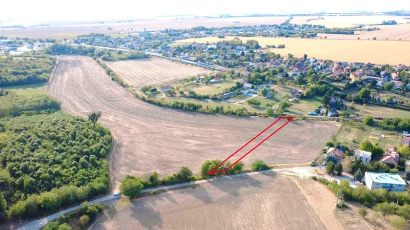 Podhájska - 2.084 m2 POZEMOK na okraji obce - Poľnohospodárske a lesné pozemky v Podhájskej, okolité polia a vzdialené budovy.