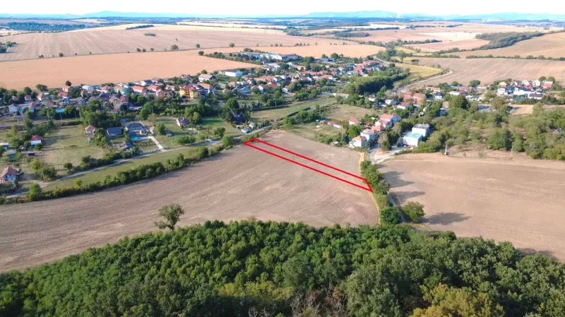 Podhájska - 2.084 m2 POZEMOK na okraji obce - Letecký pohľad na poľnohospodárske a lesné pozemky v Podhájskej, s dedinou v pozadí.