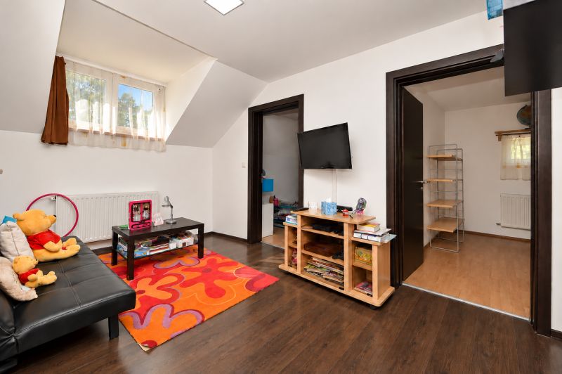 Predaj 4i dom, 52 m2 garáž, 518 m2 pozemok, Mosonmagyaróvár - Obývacia izba s pestrým kobercom a televízorom, podlaha s dreveným dekorom v rodinnom dome.