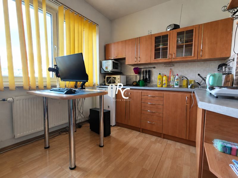REZERVOVANÉ Na predaj 1 izbový byt Martin – Podháj, ulica Timravy - Kuchyňa v 1-izbovom byte s podlahou s dreveným dekorom a žltými závesmi.