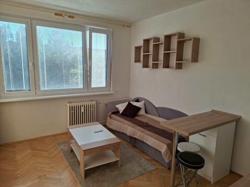 DOBRÉ REALITY-pekná garsónka na prenájom, sídl. Kopanice, Prievidza - Garsónka s podlahou s dreveným dekorom, pohovkou, stolíkom a závesnou policou.