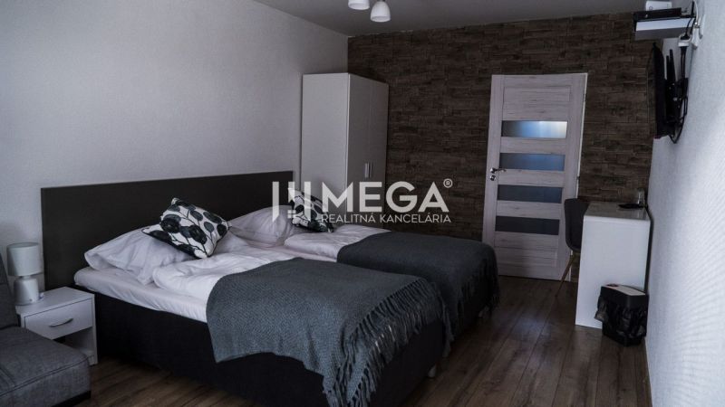 Na predaj nehnuteľnosť - zabehnutý penzión v centre mesta Humenné - Interiér izby s dvomi posteľami, stena s dekorom kameňa, podlaha s dreveným dekorom.