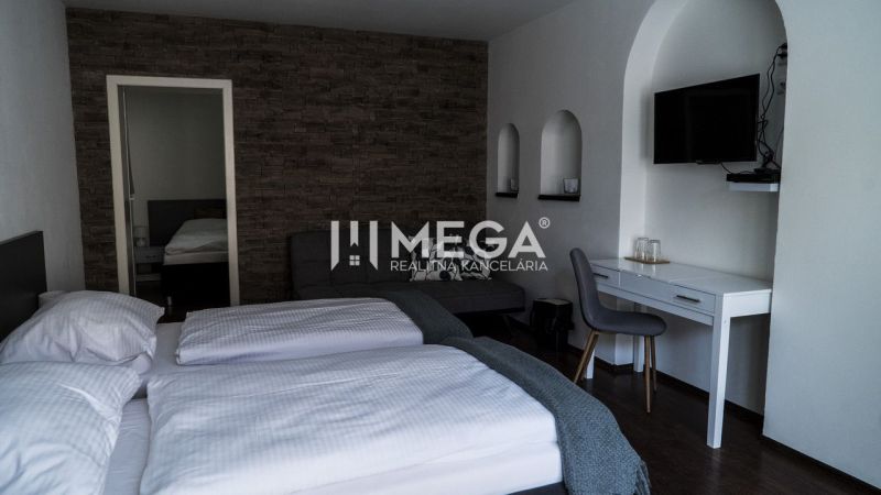Na predaj nehnuteľnosť - zabehnutý penzión v centre mesta Humenné - Hotelová izba so stenou z obkladov, podlaha s dreveným dekorom a písacím stolom.