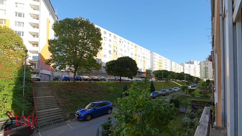 Praktický 3i BYT s obľúbenou dispozíciou - Rozkvet - PB - Sídlisko Rozkvet v Považskej Bystrici s bytovými domami a zaparkovanými autami.