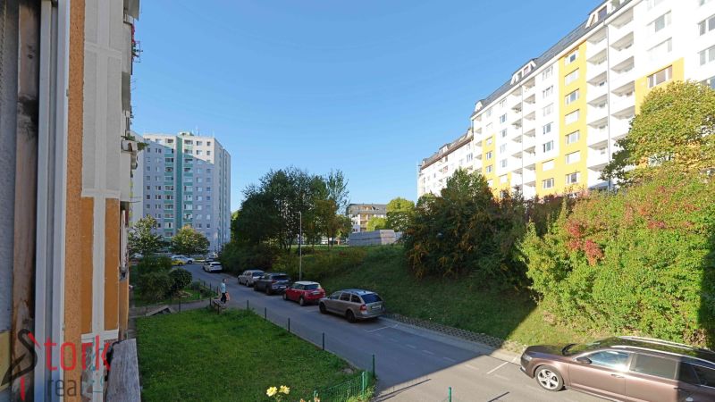 Praktický 3i BYT s obľúbenou dispozíciou - Rozkvet - PB - Ulica Rozkvet, Považská Bystrica, s bytovými domami a zaparkovanými autami pri 3-izbovom byte.