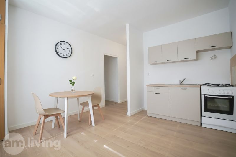 REZERVOVANÉ 1 izbový byt s balkónom - až 41m² N. DUBNICA - Kuchyňa v 1-izbovom byte s podlahou s dreveným dekorom, jedálenským stolom a hodinami.