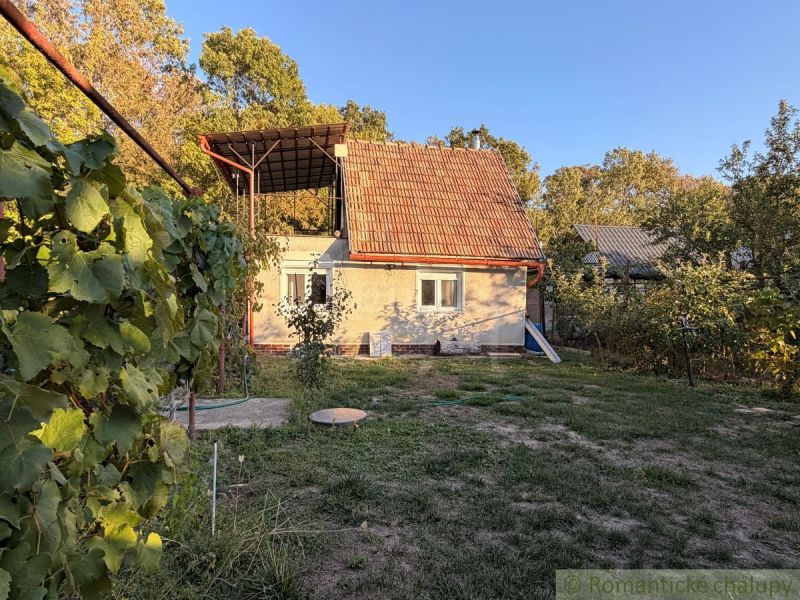 Záhrada s murovanou chatkou po rekonštrukcii iba 200 m od rieky Nitra - Chata v Nových Zámkoch s terasou, obklopená prírodou a viničom na pozadí lesa.