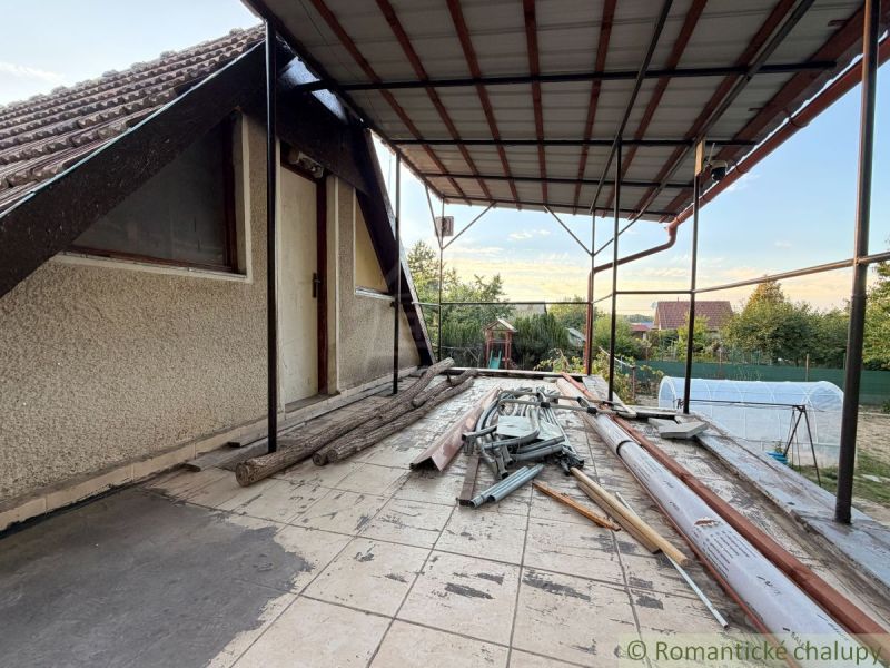 Záhrada s murovanou chatkou po rekonštrukcii iba 200 m od rieky Nitra - Terasa chaty v Nových Zámkoch s neporiadkom a stavebným materiálom, pokojná záhrada v pozadí.