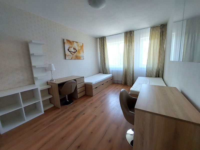 PRENÁJOM : MODERNÝ 3 IZBOVÝ BYT S TERASOU A GARÁŽOVÝM STÁTÍM, BELVEDER - Izba s dvoma posteľami, stolmi a podlahou s dreveným dekorom v 3-izbovom byte.