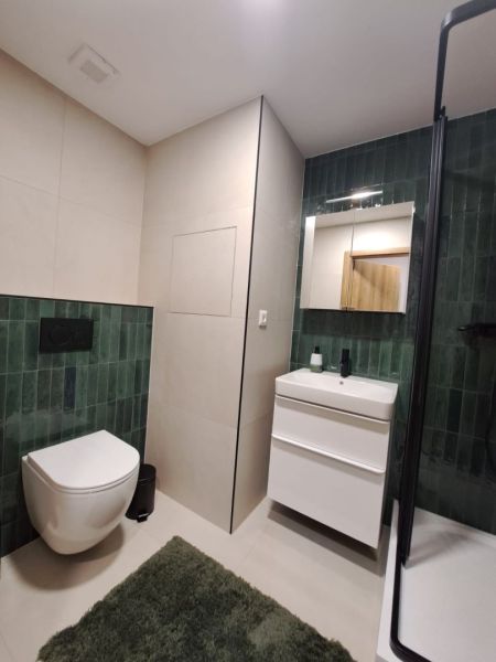 Prenájom kompletne zrekonštruovaného 2-izbového bytu s balkónom - Kúpeľňa v 2-izbovom byte s tmavo zelenými obkladačkami a bielym sanitárnym zariadením.