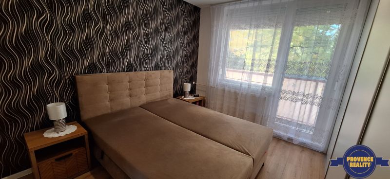 REZERVOVANÉ: 3 izbový byt + 2x balkón, komplet.rekonštr. - KOMÁRNO - Spálňa s čalúnenou posteľou, vzorovaná tapeta, záclony, podlaha s dreveným dekorom.