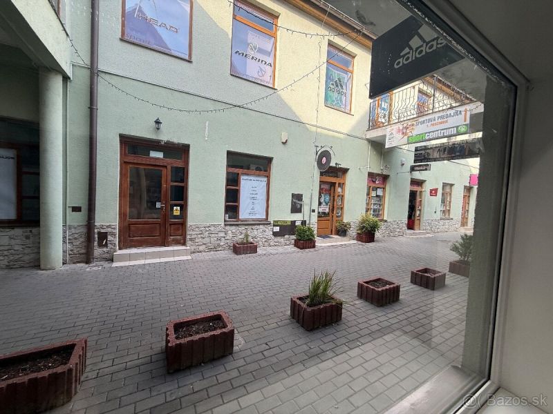 Obchodný priestor - TOP PONUKA V CENTRE - Obchodné priestory v Topoľčanoch s kamenným obkladom a kvetináčmi na vydláždenej ulici.