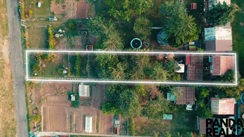 3.izbový byt so záhradou /420 m²/ a chatkou BOŠANY - Záhrada na ulici Janka Kráľa v Bošanoch, obklopená stromami a drobnými stavbami.