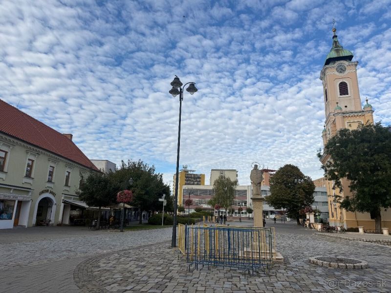Lukratívny obchodný priestor v Centre Topolčian   - Obchodné priestory v Topoľčanoch s dláždeným námestím a kostolom v pozadí.