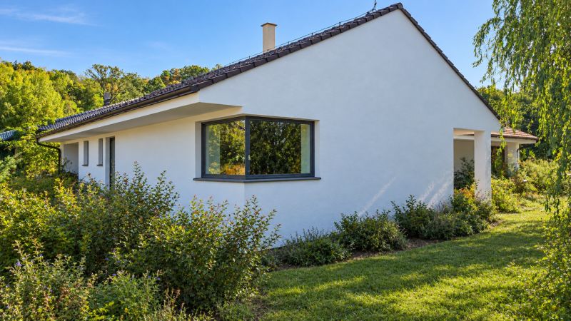 MODERNÝ 6-IZBOVÝ BUNGALOV S TERASOU A POZEMKOM 884 m² – RATNOVCE - Rodinný dom v Ratnovciach obklopený zeleňou, s veľkými oknami a jednoduchou bielou fasádou.