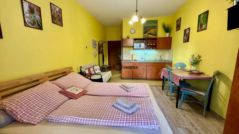 NA PREDAJ investičný apartmán v Podhájskej - Žlté steny, kuchynská linka, jedálenský stôl, posteľ a podlaha s dreveným dekorom v Rekreačnom apartmáne.