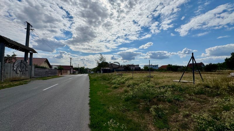 NA PREDAJ Stavebný pozemok v obci Golianovo - Cesta v Golianove obklopená pozemkami na bývanie pod oblakmi na modrom nebi.