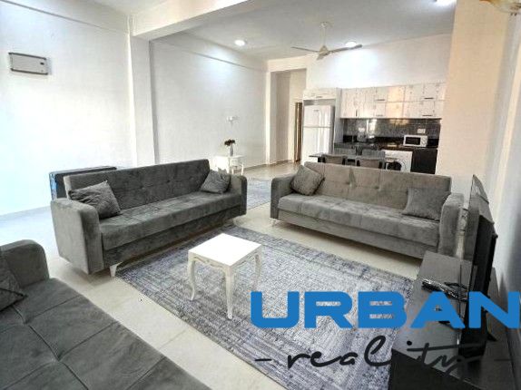 2-IZBOVÝ CONDO APARTMÁN PRI PLÁŽI, MBWENI, ZANZIBAR - Obývačka s tromi sivými pohovkami, stolíkom a kuchyňou v 2-izbovom byte.
