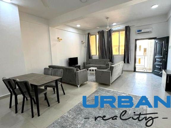 2-IZBOVÝ CONDO APARTMÁN PRI PLÁŽI, MBWENI, ZANZIBAR - 2-izbový byt s tmavými gaučmi, jedálenským stolom a televízorom, podlaha s dreveným dekorom.