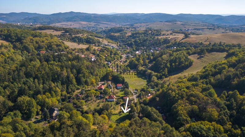 Predaj, rekreačné pozemky Štiavnické Bane - Letecký pohľad na Rekreačné pozemky v Štiavnických Baniach obklopené zelenými lesmi a kopcami.