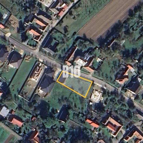Rovinatý Pozemok určený k výstavbe domu - Letecký pohľad na pozemok na bývanie v Moravskom Lieskovom s viditeľnou ulicou a budovami.