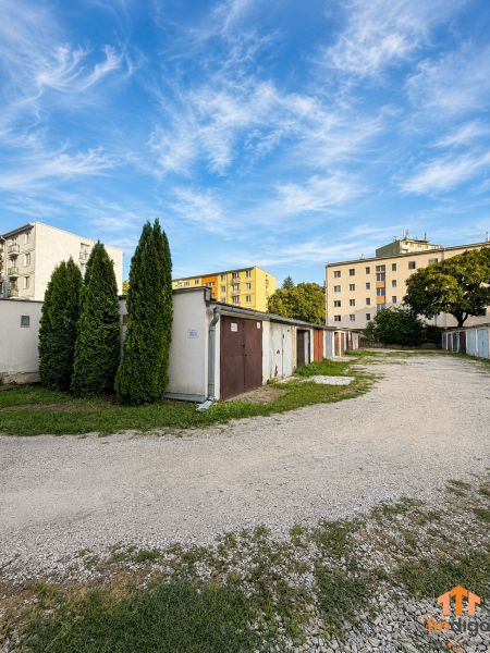 PRENÁJOM - Murovaná garáž 18 m² –  Nitra - Garáže na Schurmannovej ulici v Nitre s obytnými domami a modrou oblohou.