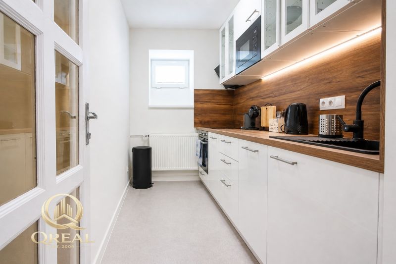 **Hotový priestor. Povolené ubytovanie. Pripravené zarábať**Airbnb** - Úzka kuchyňa s bielymi skrinkami, drevený dekor pultu, zabudovaná mikrovlnka.