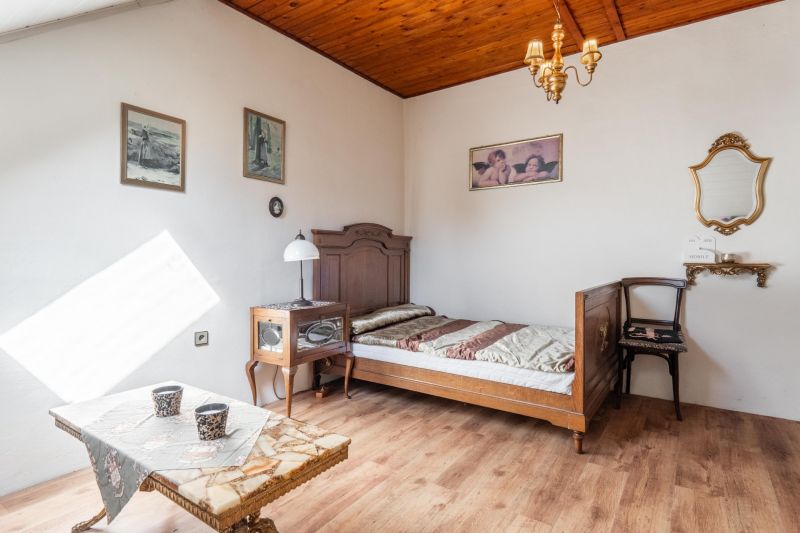 I VILA REIM – Exkluzívna investičná príležitosť  - Interiér chaty s dreveným dekorom podlahy, jednoduchá posteľ a starožitné kreslo.