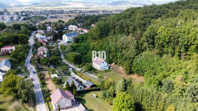 Priestranný 5-izbový rodinný dom na veľkom pozemku pri lese - Letecký pohľad na rodinné domy v obci Ladce, obklopené zelenými svahmi a lesom.