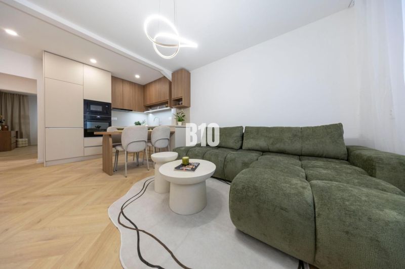NOVO ZREKONŠTRUOVANÝ 4-IZBOVÝ BYT V TICHOM PROSTREDÍ - 78 m² - NOVÉ ME - Obývacia izba v 4-izbovom byte s podlahou s dreveným dekorom a zelenou sedačkou.