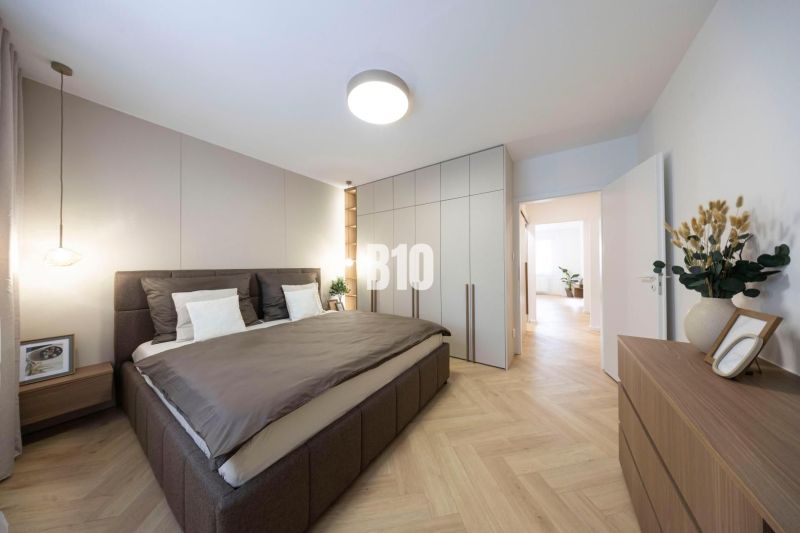 NOVO ZREKONŠTRUOVANÝ 4-IZBOVÝ BYT V TICHOM PROSTREDÍ - 78 m² - NOVÉ ME - Spálňa v 4-izbovom byte s podlahou s dreveným dekorom, svetlým nábytkom a rastlinou.